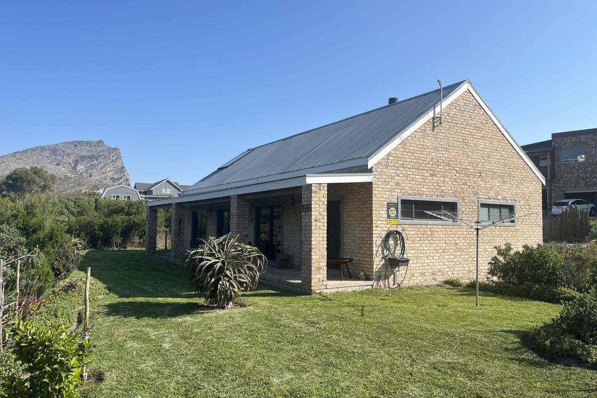 A well-maintained single-story brick house featuring a metal roof, a covered patio area, and a spacious surrounding garden with mountain views.