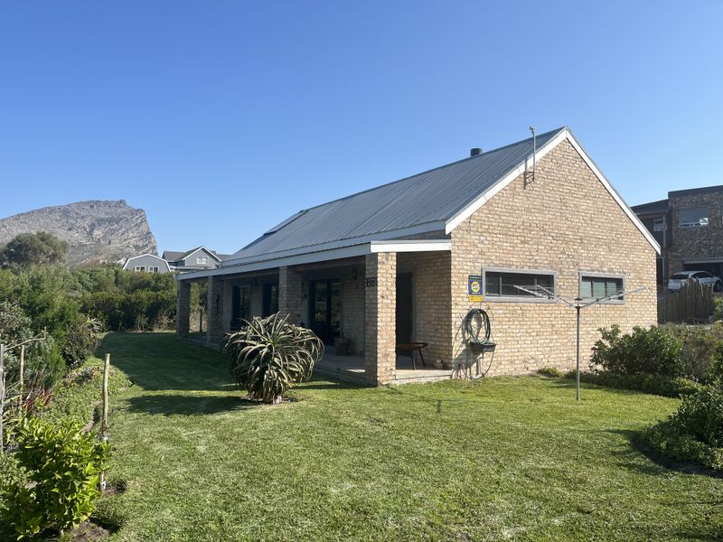 A well-maintained single-story brick house featuring a metal roof, a covered patio area, and a spacious surrounding garden with mountain views.