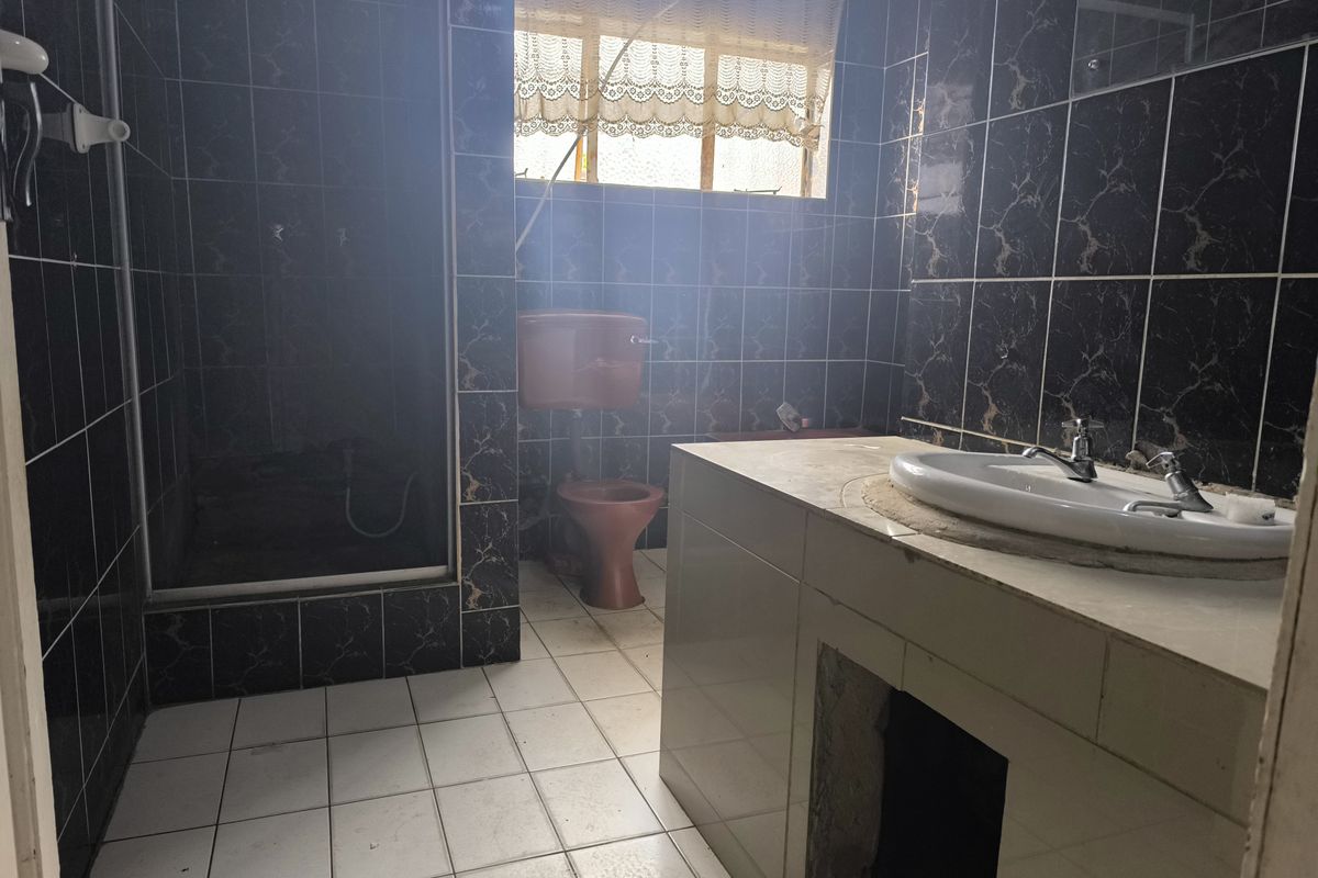 A dated bathroom featuring dark marble-effect wall tiles, a vanity basin, and a separate shower enclosure, requiring modernization to improve functionality and aesthetic appeal.