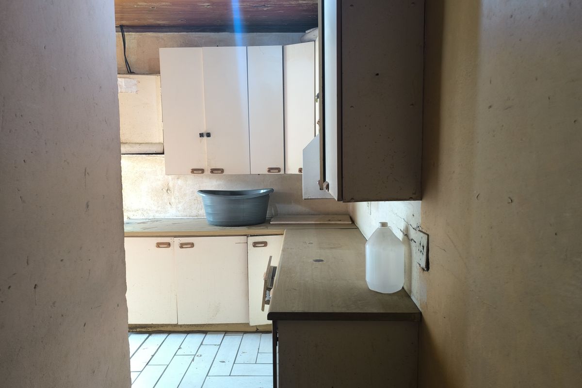 A dated kitchen area featuring original built-in cabinetry, laminate countertops, and tiled flooring, requiring significant cosmetic updates and refurbishment.