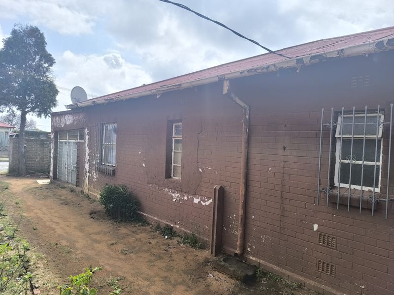 Side view of the property showing brick exterior walls, metal roofing, and security bars on windows, requiring maintenance on paint and structural finishes.