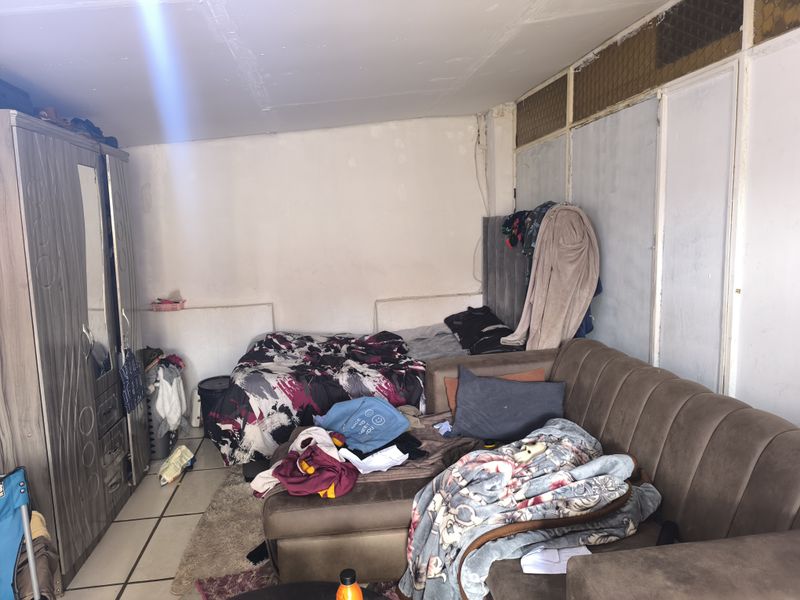 A bedroom featuring tiled flooring and a built-in wardrobe, currently showing signs of wear and requiring cosmetic updates to the walls and ceiling.