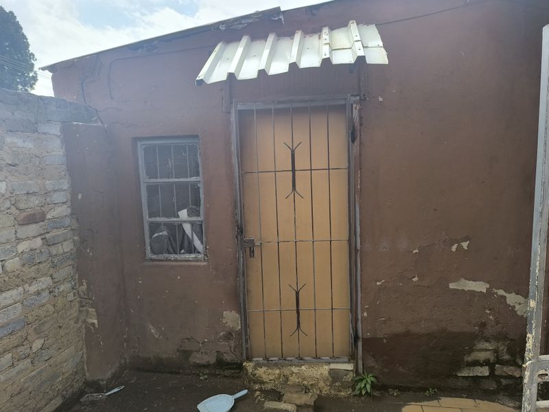Exterior view of a rear building entrance featuring a security gate, metal awning, and visible wear to the plaster and masonry finishes.
