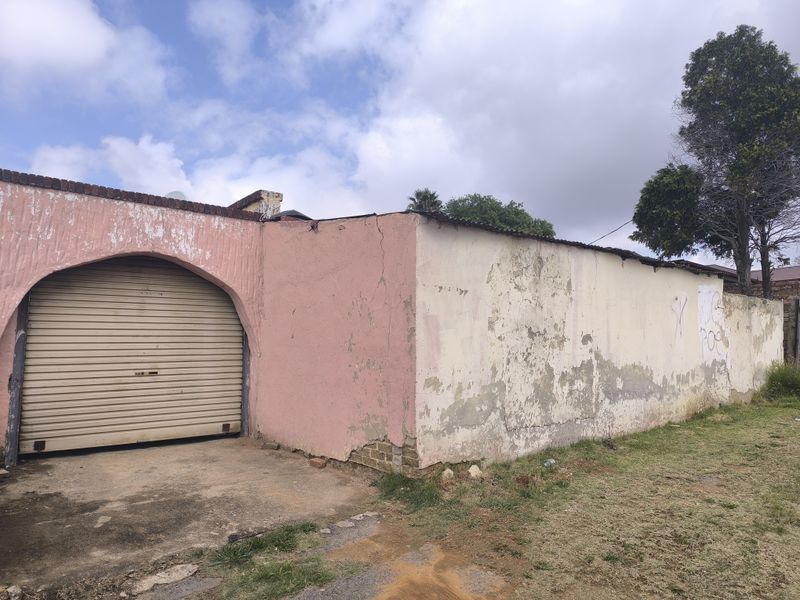 Exterior view of a property featuring a roller shutter garage door and a masonry boundary wall showing significant signs of weathering and surface damage.