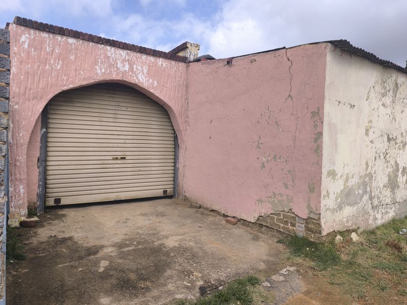 A detached garage structure featuring a roller shutter door and an arched entrance, currently showing significant signs of exterior wear and structural weathering.