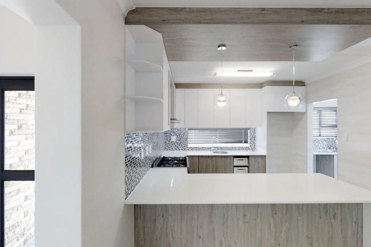 Modern kitchen featuring white cabinetry, quartz countertops, mosaic tile backsplash, gas hob, and stylish pendant lighting with a unique dropped ceiling detail.