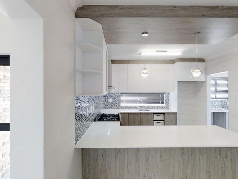 Modern kitchen featuring white cabinetry, quartz countertops, mosaic tile backsplash, gas hob, and stylish pendant lighting with a unique dropped ceiling detail.