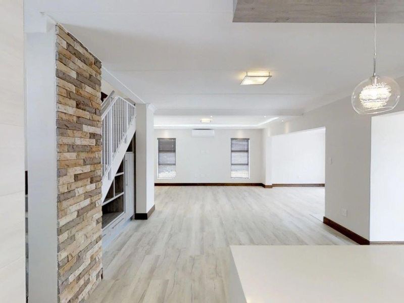 Spacious open-plan living area featuring a modern stone accent wall, light laminate flooring, built-in staircase storage, and contemporary recessed lighting.