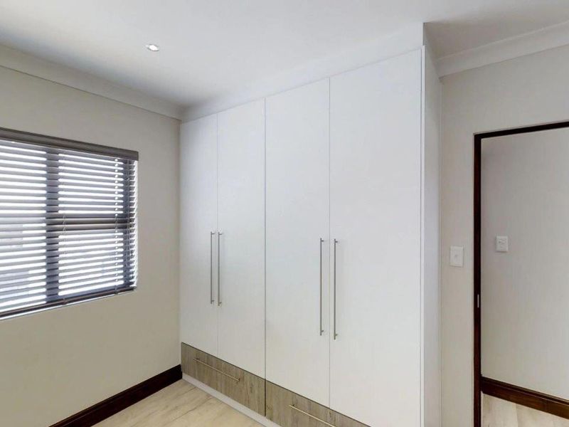 A clean, modern bedroom featuring built-in cupboards with wood-look base drawers, neutral walls, and venetian blinds.