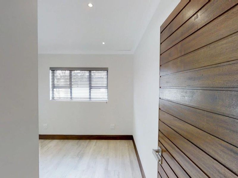 A bright, empty bedroom featuring modern laminate flooring, recessed downlights, and a distinctive horizontal slatted timber door.