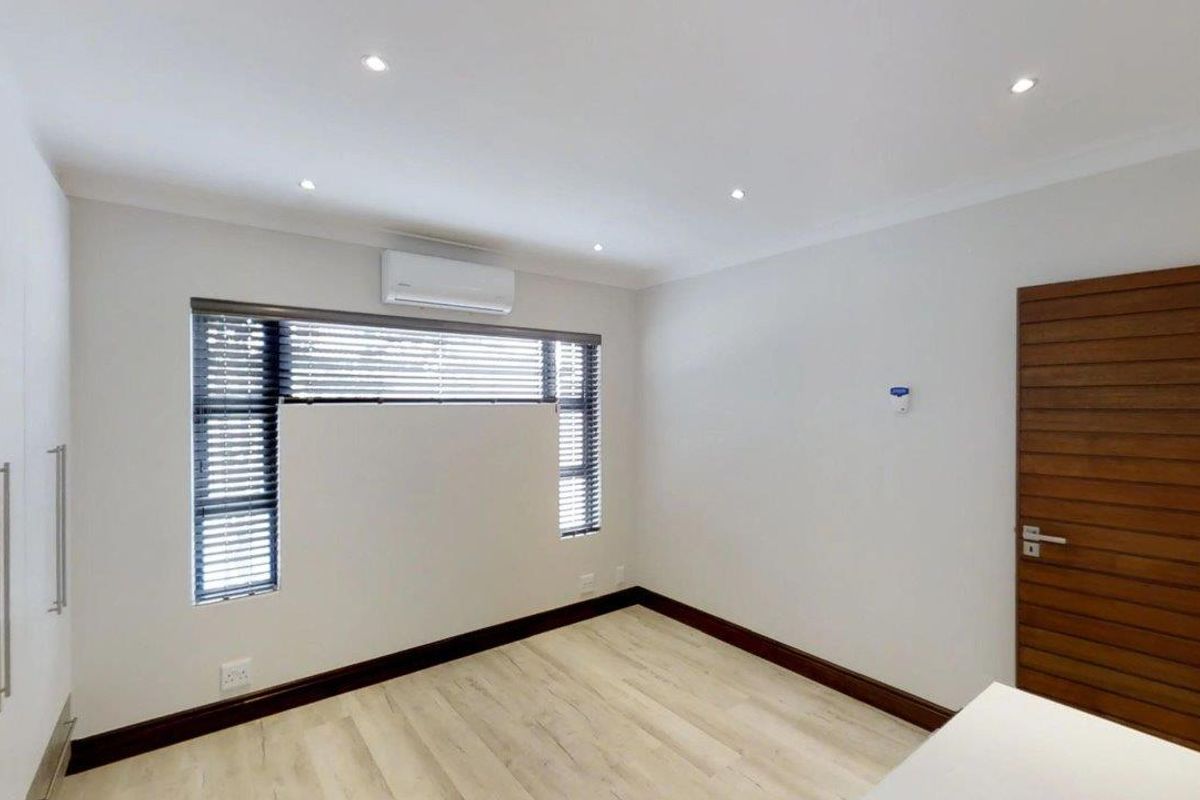 A bright, modern bedroom featuring laminate flooring, built-in cupboards, recessed lighting, and an air conditioning unit.