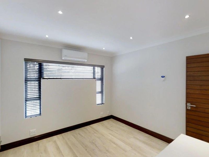 A bright, modern bedroom featuring laminate flooring, built-in cupboards, recessed lighting, and an air conditioning unit.