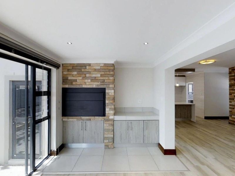Spacious open-plan living area featuring a built-in fireplace with stone cladding, modern cabinetry, tiled floors, and large sliding doors leading to the exterior.