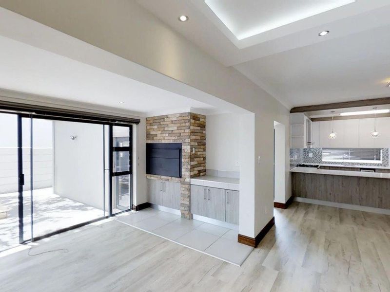 Modern open-plan living area featuring a built-in fireplace with stone cladding, sleek kitchen cabinetry, and large sliding doors leading to an outdoor patio.