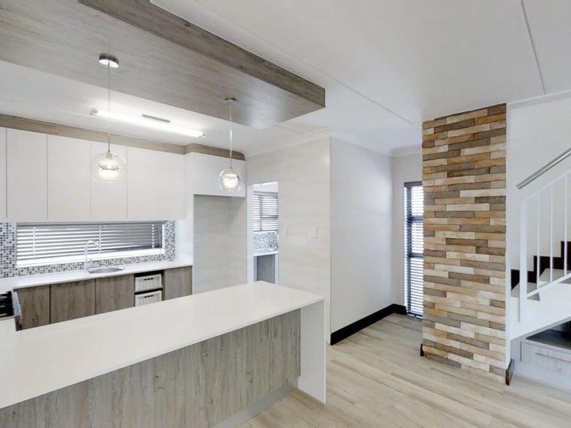 Modern open-plan kitchen featuring sleek cabinetry, stone countertops, and a striking stone feature wall adjacent to a contemporary staircase.