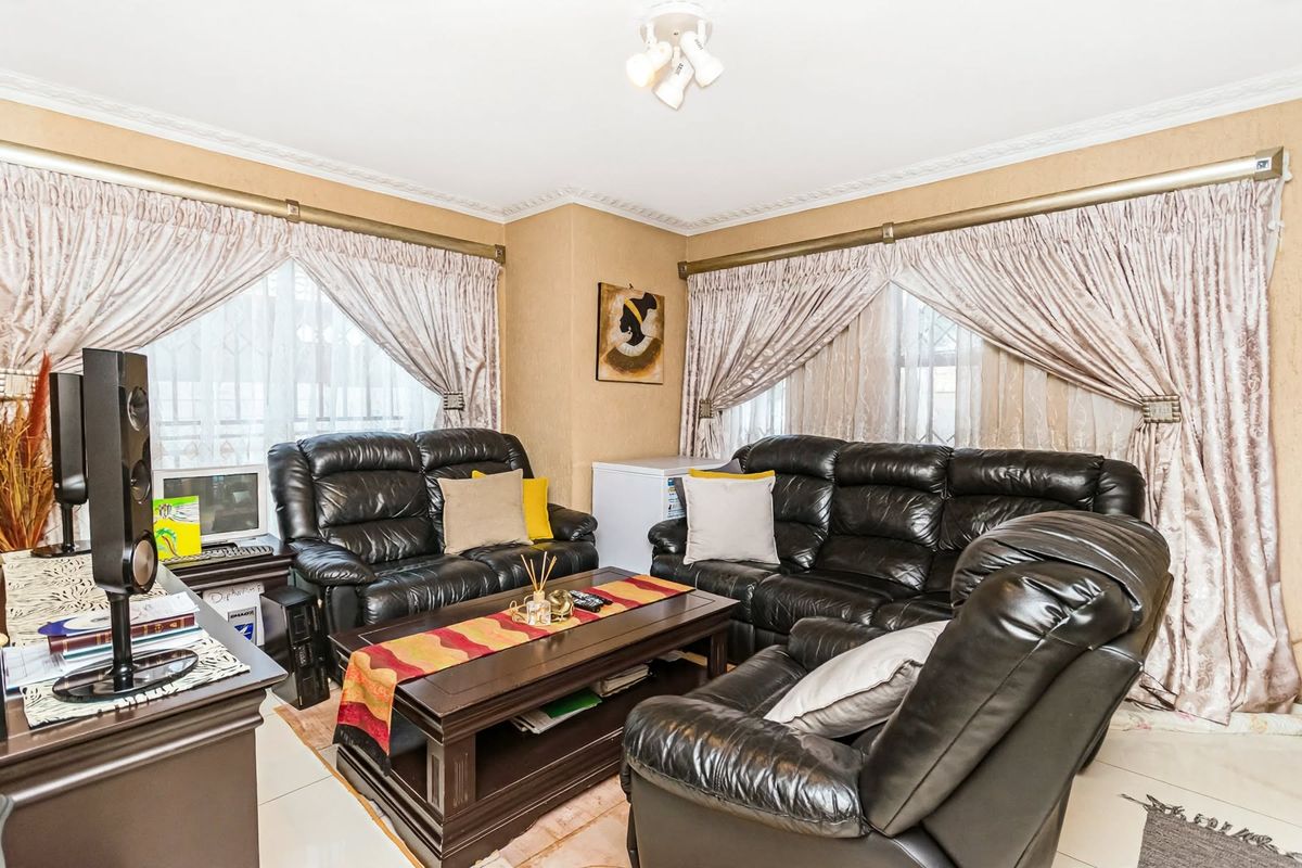 A comfortable living room featuring tiled flooring, decorative crown molding, and dual windows with installed curtain rods.