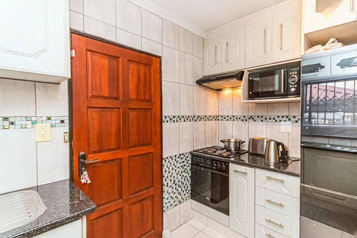 Compact kitchen featuring built-in cabinetry, granite countertops, a tiled backsplash, and integrated appliances including an oven, hob, and microwave.