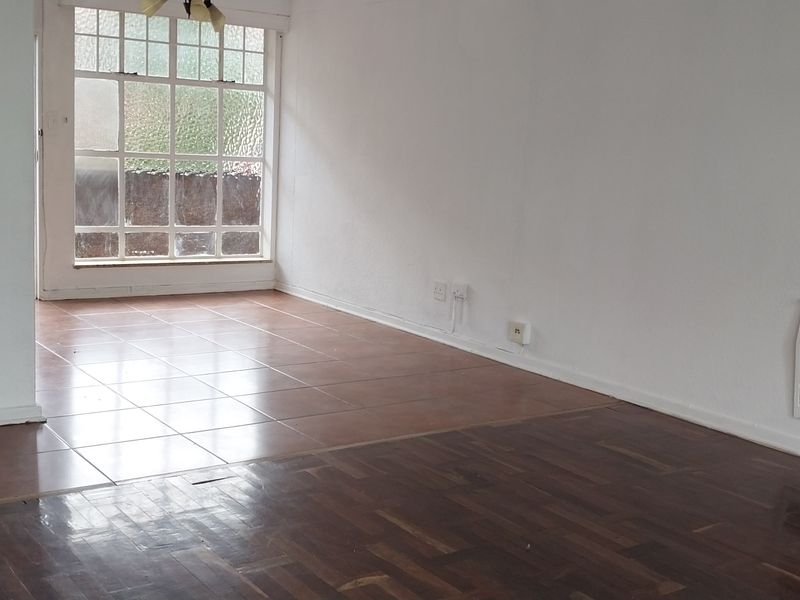 An empty living room featuring a combination of parquet and ceramic tile flooring, a wall-mounted heater, and a large multi-pane window.