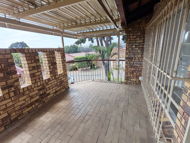 A covered outdoor patio featuring brick walls, paved flooring, and metal security gates, offering a functional space for outdoor relaxation.