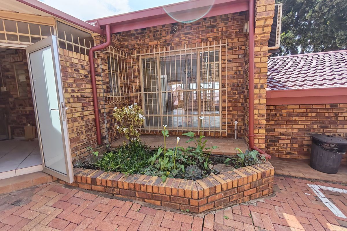 Rear courtyard area featuring face brick construction, paved flooring, a built-in brick planter box, and secure access points with metal security bars.