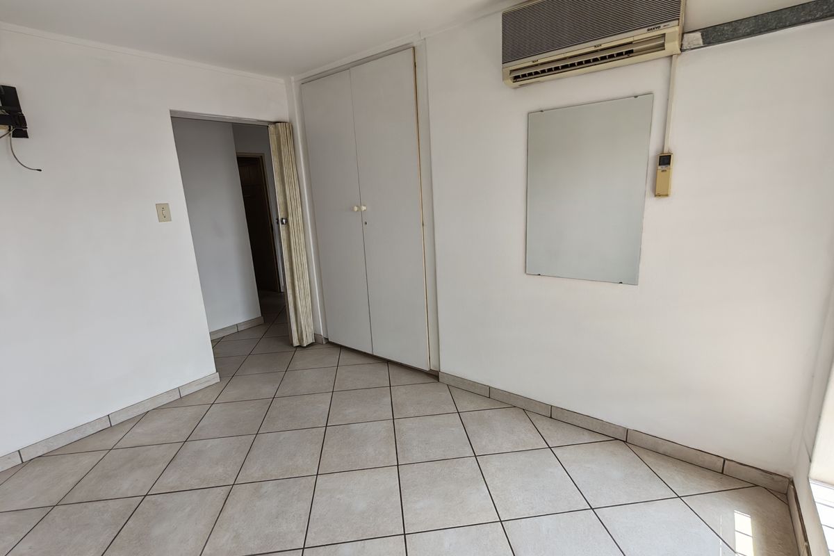 An empty bedroom featuring tiled flooring, built-in cupboards, and a wall-mounted air conditioning unit, offering a blank canvas for renovation.