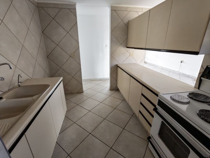 A functional kitchen featuring tiled flooring, neutral cabinetry, a double basin sink, and a freestanding stove with a tiled splashback.