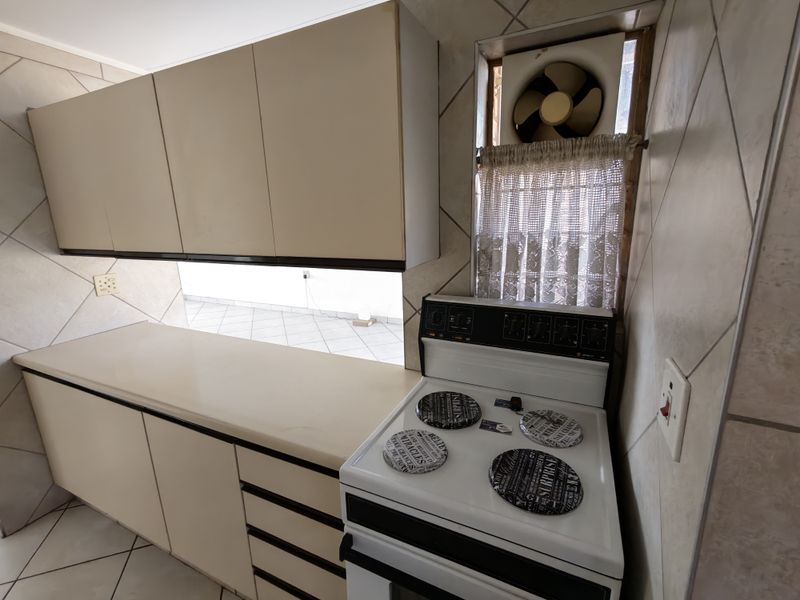 A dated kitchen featuring original cabinetry, laminate countertops, and a freestanding stove, with ceramic tiling throughout.