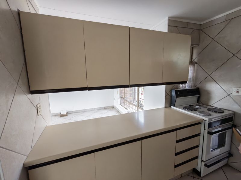 A functional kitchen featuring built-in cabinetry, laminate countertops, and a freestanding stove, finished with classic diagonal ceramic wall tiling.
