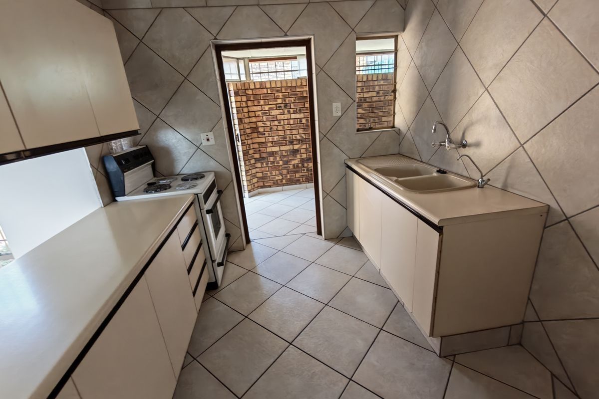 A functional kitchen featuring tiled flooring, built-in cabinetry, a double basin sink, and a freestanding stove, with direct access to an outdoor area.