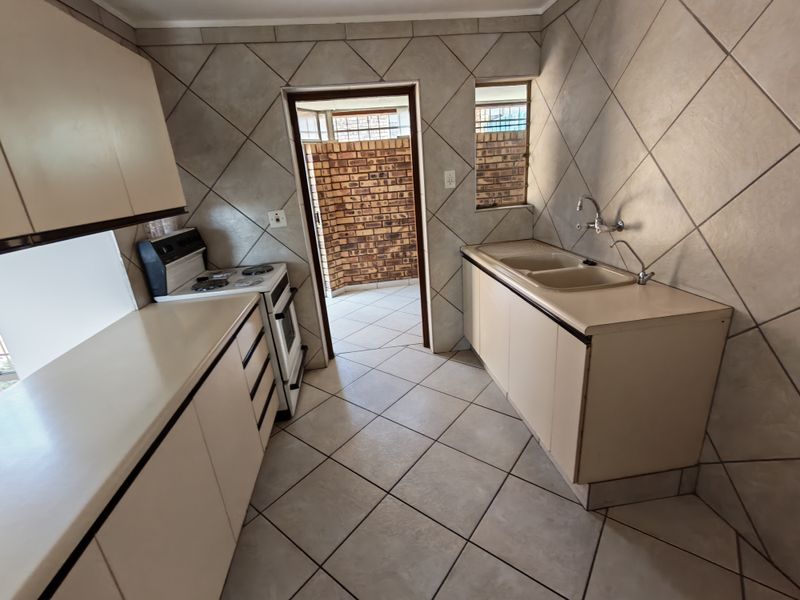 A functional kitchen featuring tiled flooring, built-in cabinetry, a double basin sink, and a freestanding stove, with direct access to an outdoor area.