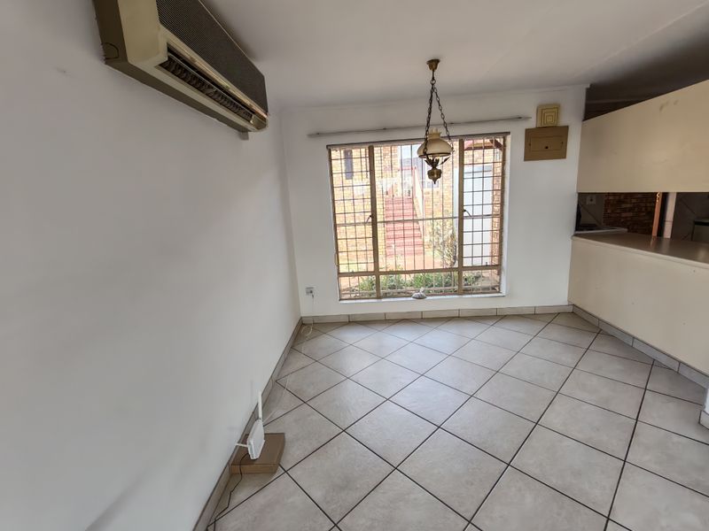 An open-plan living and kitchen area featuring ceramic tiled flooring, a wall-mounted air conditioner, and a window with security bars.