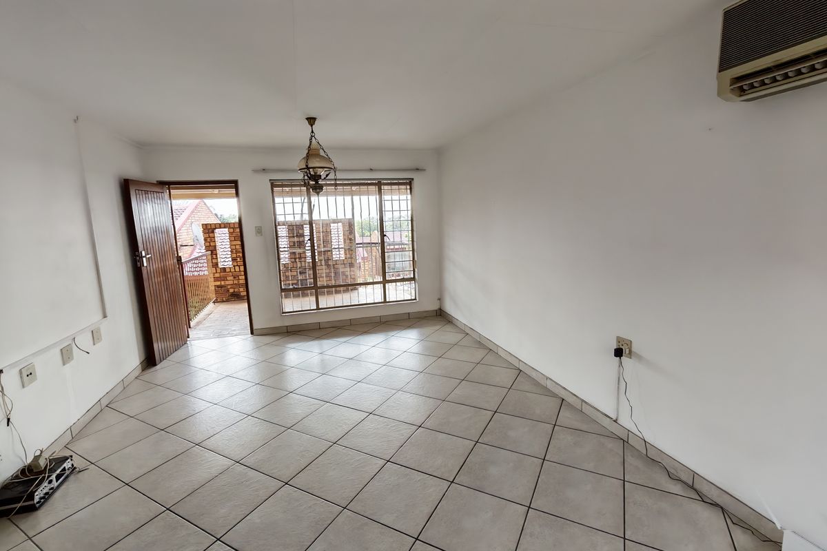 An empty living room featuring ceramic floor tiles, a wall-mounted air conditioning unit, and direct access to an outdoor balcony area.