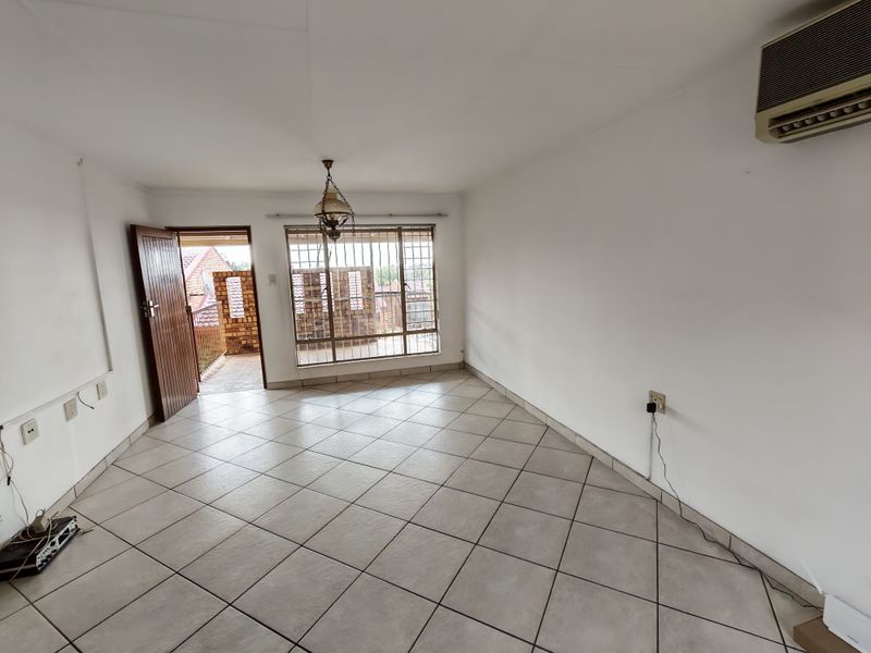 An empty living room featuring ceramic floor tiles, a wall-mounted air conditioning unit, and direct access to an outdoor balcony area.