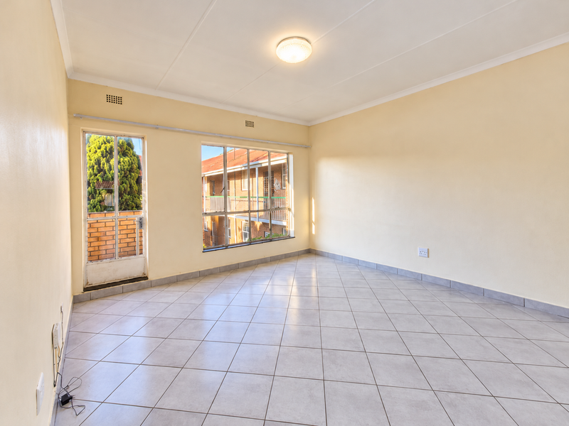 A bright, empty living room featuring neutral tiled flooring, large windows providing natural light, and direct access to an outdoor balcony area.