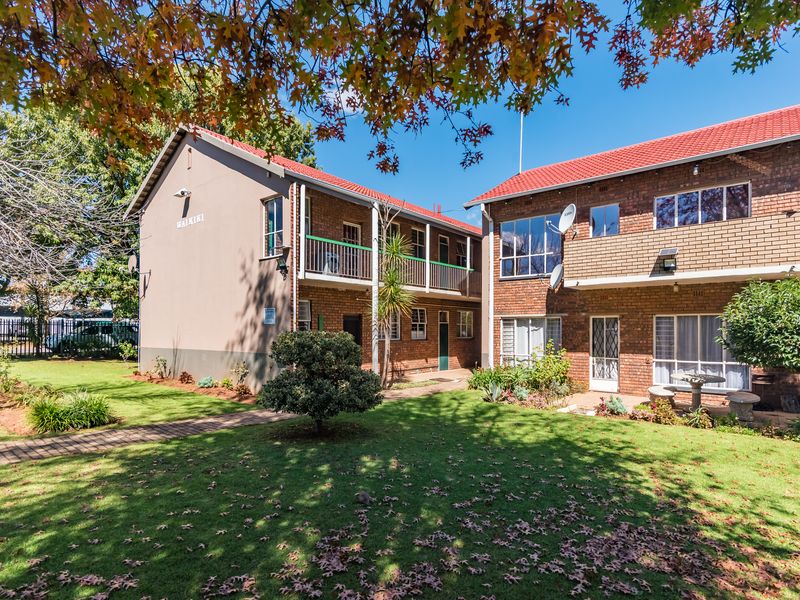 Exterior view of a multi-story apartment complex featuring brick facades, tiled roofing, balconies, and a well-maintained communal garden area.