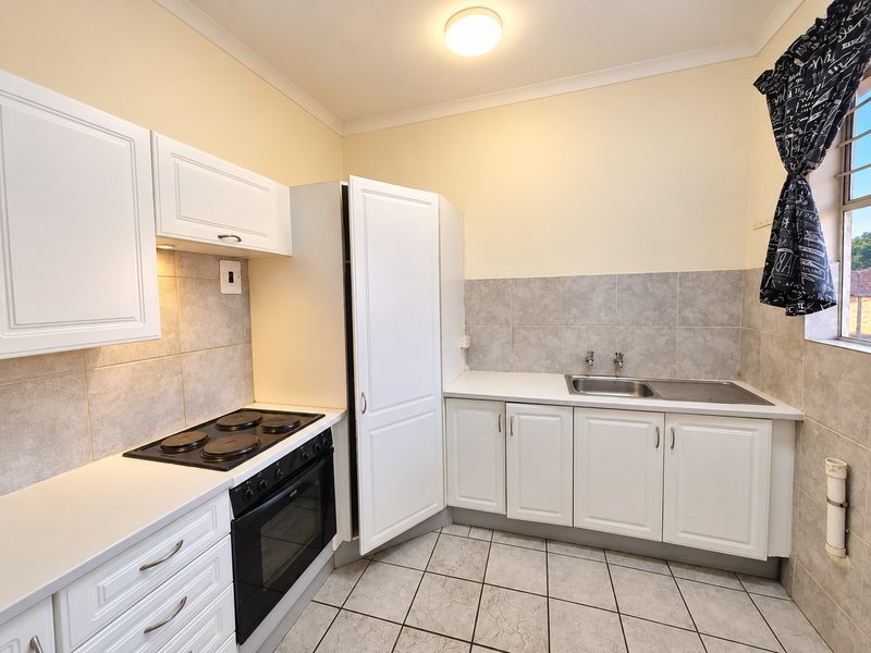 A functional kitchen featuring white cabinetry, a built-in electric oven and hob, tiled backsplash, and a stainless steel sink.
