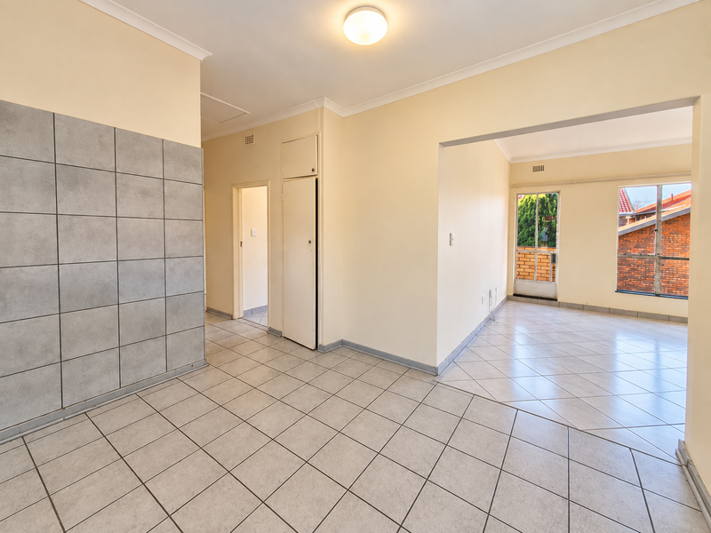 An empty open-plan living area featuring neutral tiled flooring, a tiled feature wall, and natural light through aluminium-framed windows.