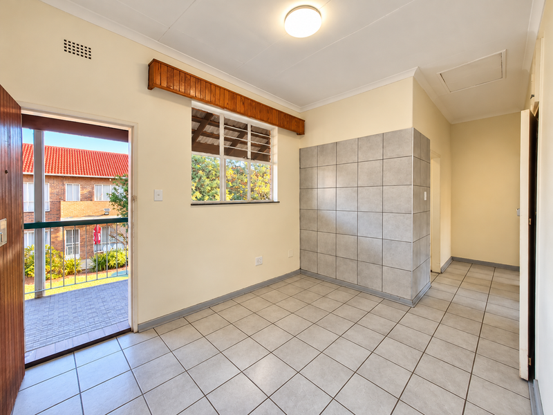 An empty, tiled living area featuring a tiled accent wall, ceiling light, and direct access to an outdoor balcony.
