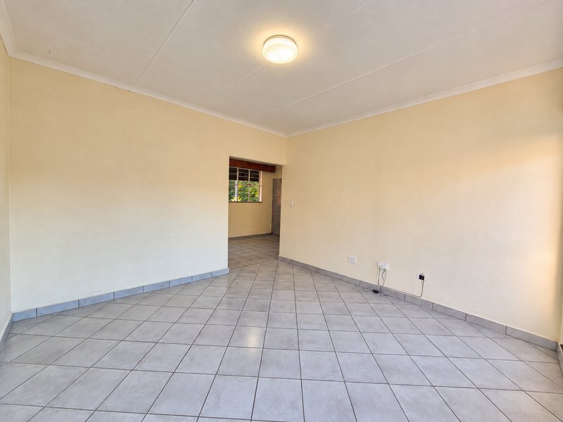 A spacious, empty living area featuring neutral wall paint, ceramic floor tiles, and a central ceiling light fixture.