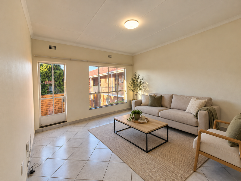 A bright living room featuring tiled flooring, large windows providing natural light, and a glass panel door leading to an outdoor area.