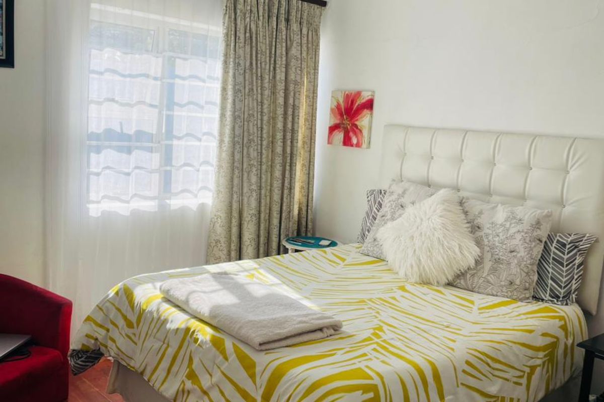 A cozy bedroom featuring warm hardwood flooring, crown molding, and natural light through a window with curtain fixtures.
