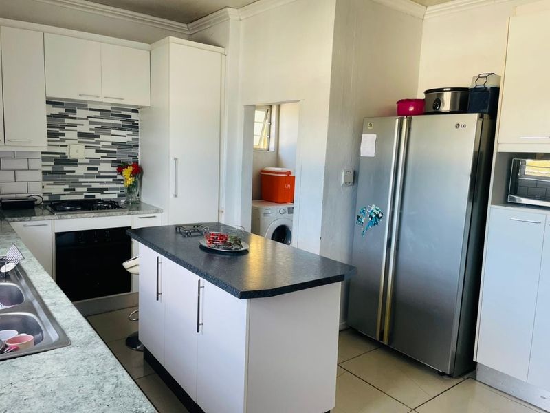 Modern kitchen featuring white cabinetry, a central island, mosaic tile backsplash, and integrated appliances, with an adjacent laundry area.
