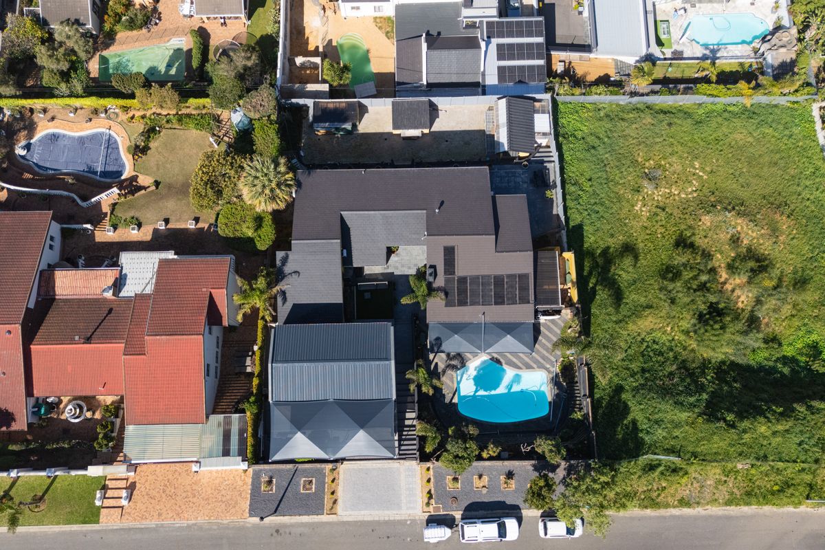 Aerial view of the property showcasing the roof structure, swimming pool, paved driveway, and surrounding garden area.