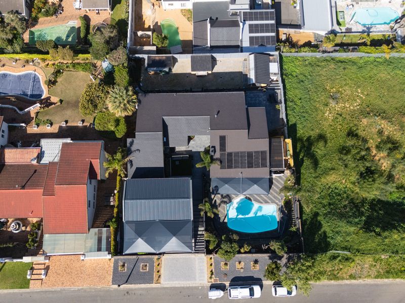 Aerial view of the property showcasing the roof structure, swimming pool, paved driveway, and surrounding garden area.