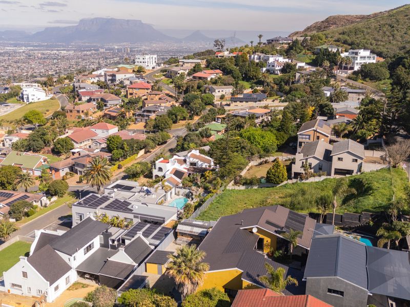 An aerial view of a residential neighborhood featuring homes with solar panels, swimming pools, and scenic mountain views in the distance.