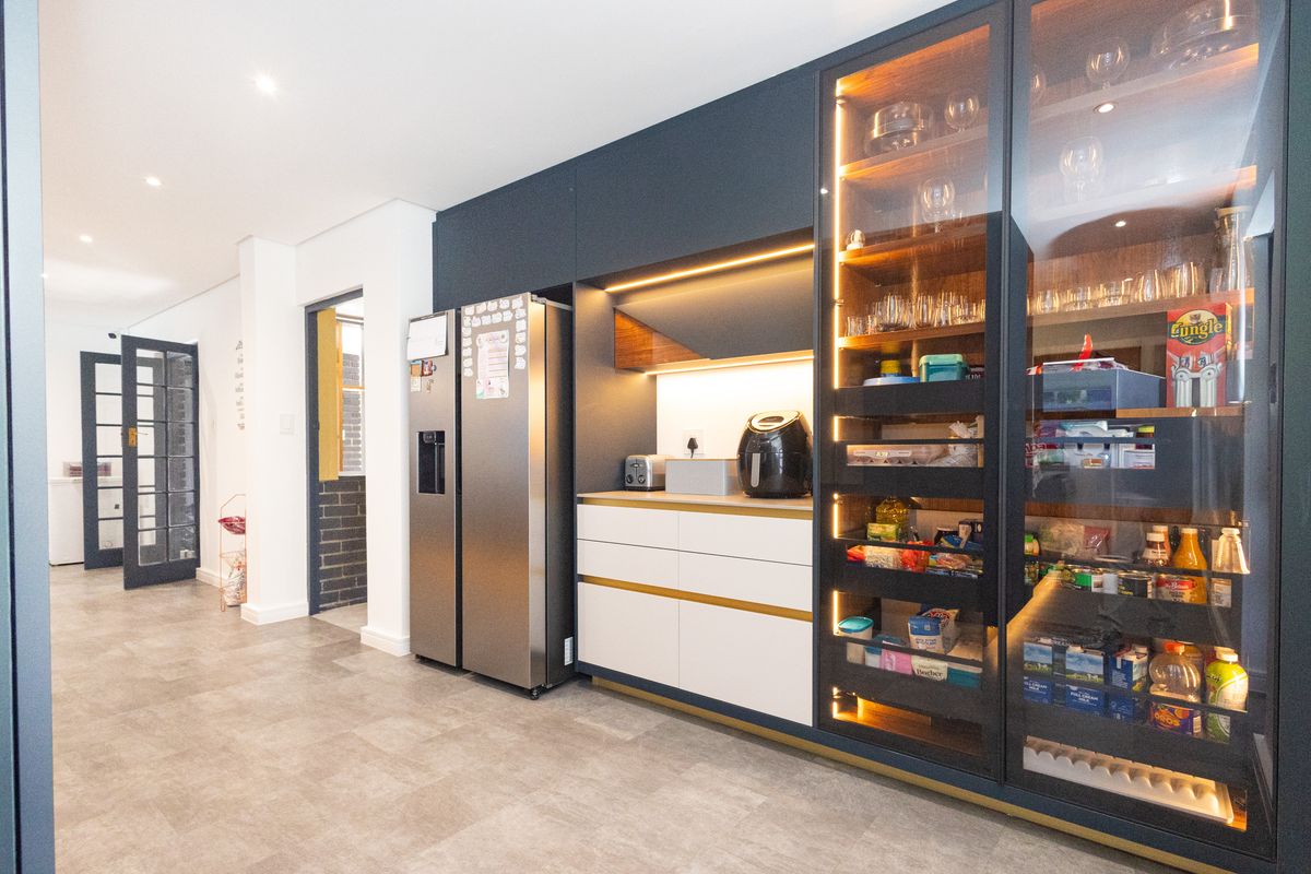 Modern kitchen featuring sleek dark cabinetry, integrated glass-front display shelving with internal lighting, and high-quality tiled flooring.