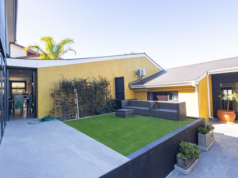 A modern outdoor patio area featuring tiled flooring, an artificial lawn section, and a retaining wall, providing a seamless transition to the interior living space.