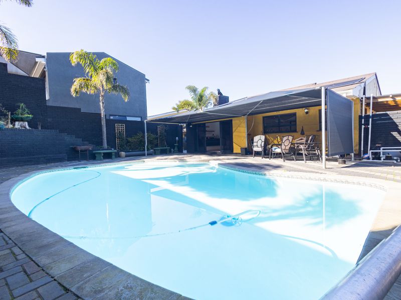 Outdoor pool area featuring a paved surround, retaining walls, and a retractable awning providing shade for the patio space.
