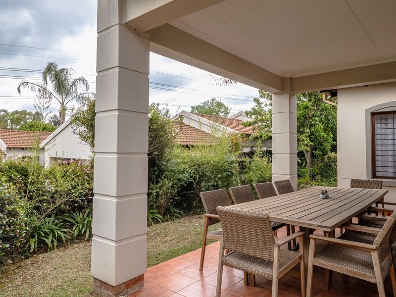A covered outdoor patio featuring tiled flooring and masonry columns, overlooking a private garden area.