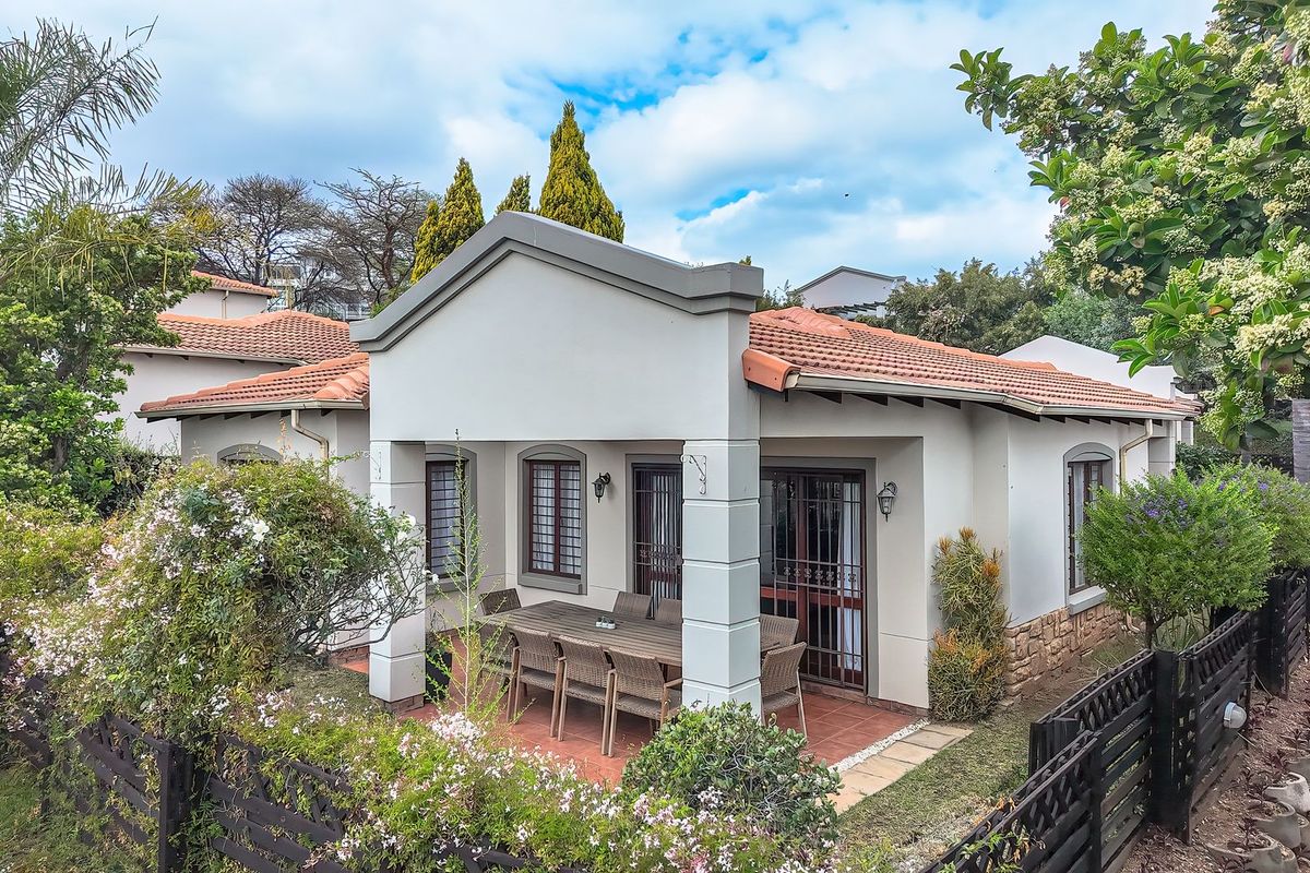 Rear view of the property featuring a covered patio area, tiled roof, and established garden surroundings with secure perimeter fencing.